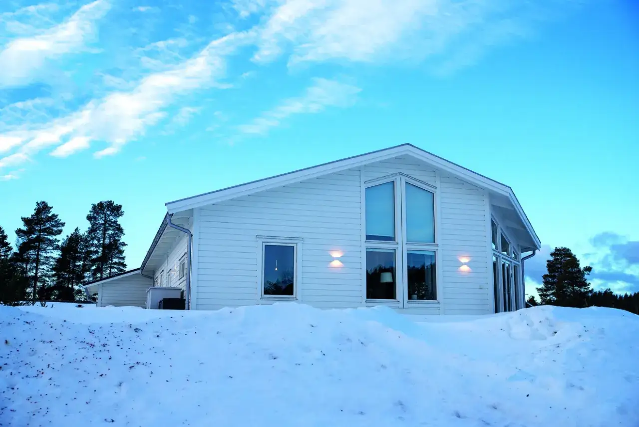 Vitt hus i sn&ouml;landskap med stora f&ouml;nster, perfekt f&ouml;r ett off grid-liv i Sverige.