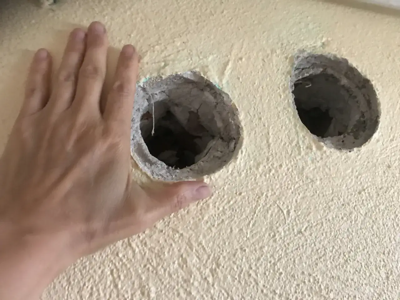 En hand h&aring;ller upp mot en gul v&auml;gg med tv&aring; stora h&aring;l. Dags att spackla h&aring;l och fixa till v&auml;ggen.