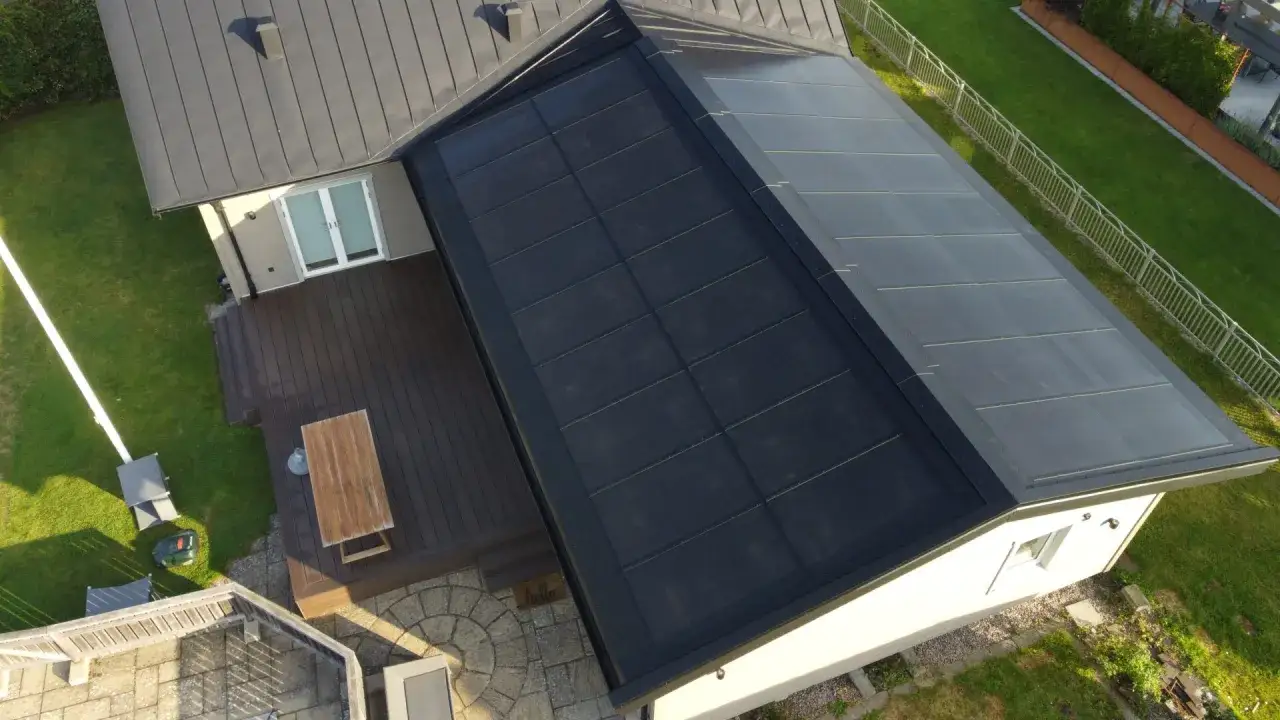 Tak med integrerade solceller eller solpaneler som täcker en stor yta. Ett modernt hus med trädäck och grönskande trädgård.
