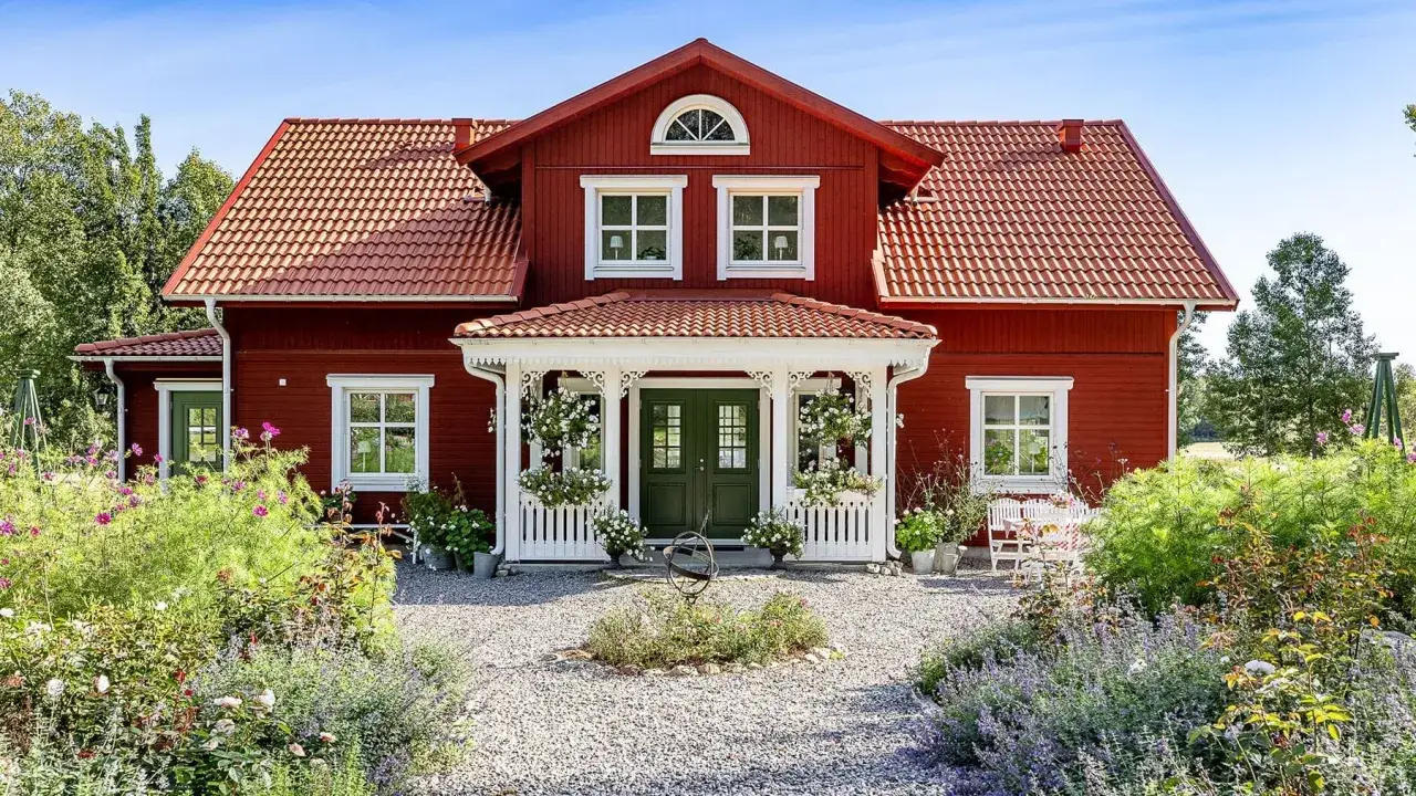 R&ouml;tt hus med vita detaljer och en vacker tr&auml;dg&aring;rd. Dr&ouml;mmen om att bygga ut gammalt hus blir verklighet h&auml;r.