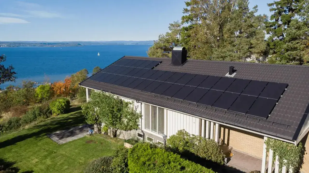 Hus med m&ouml;rka, moderna solceller p&aring; taket, vackert bel&auml;get vid en sj&ouml;. Olika typer av solceller bidrar till h&aring;llbar energi.
