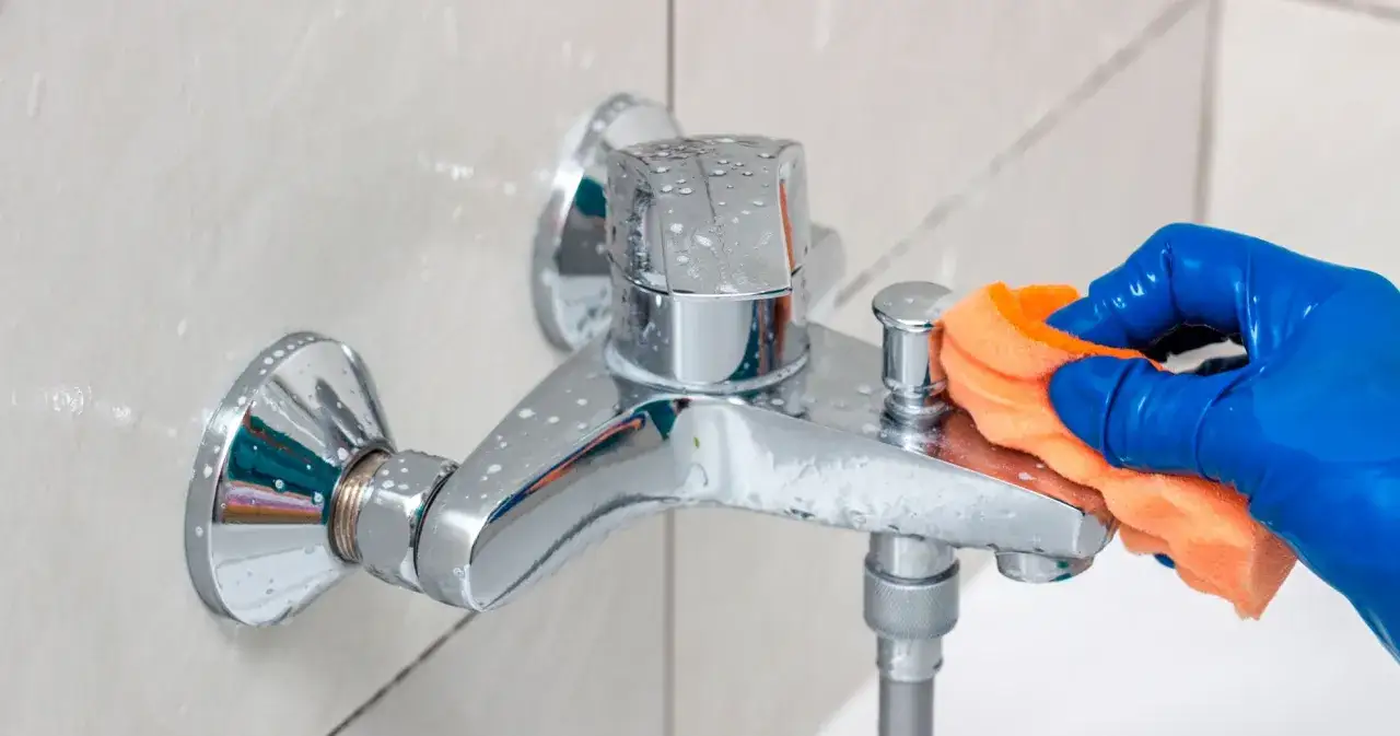 Bl&aring; gummihandske med en orange svamp putsar en kran f&ouml;r att ta bort kalk.