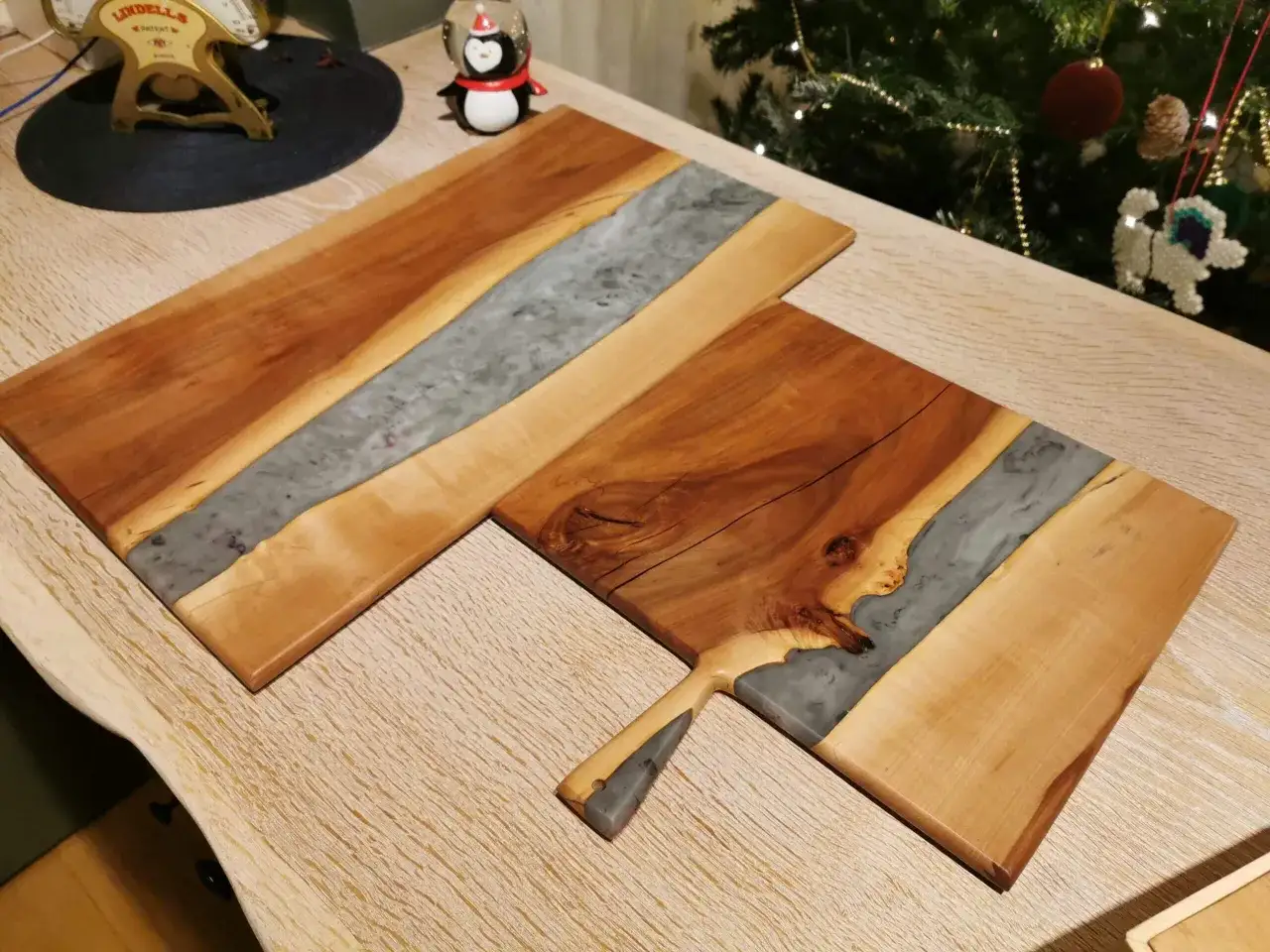 Tv&aring; vackra sk&auml;rbr&auml;dor av h&aring;rt virke med inslag av gr&aring; resin. En julgran syns i bakgrunden.