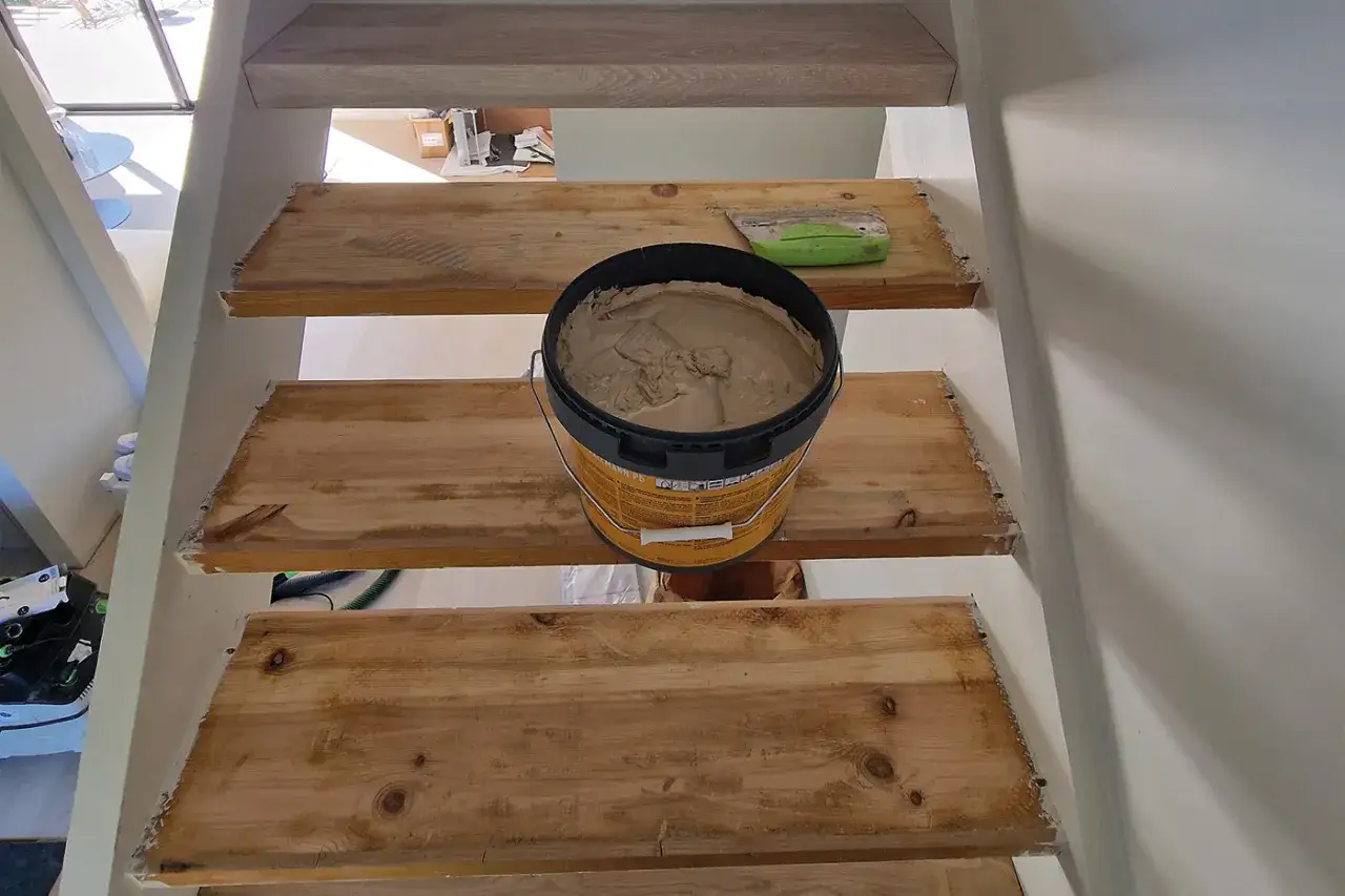 En stor hink med spackel st&aring;r p&aring; en tr&auml;trappa som ska slipas. En gr&ouml;n spackelspade ligger bredvid.