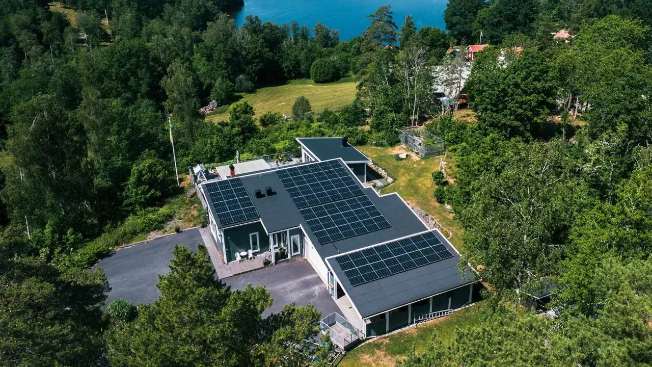 Hus med solceller i en gr&ouml;nskande svensk milj&ouml; vid en sj&ouml;. Elcertifikat solceller ger h&aring;llbar energi.