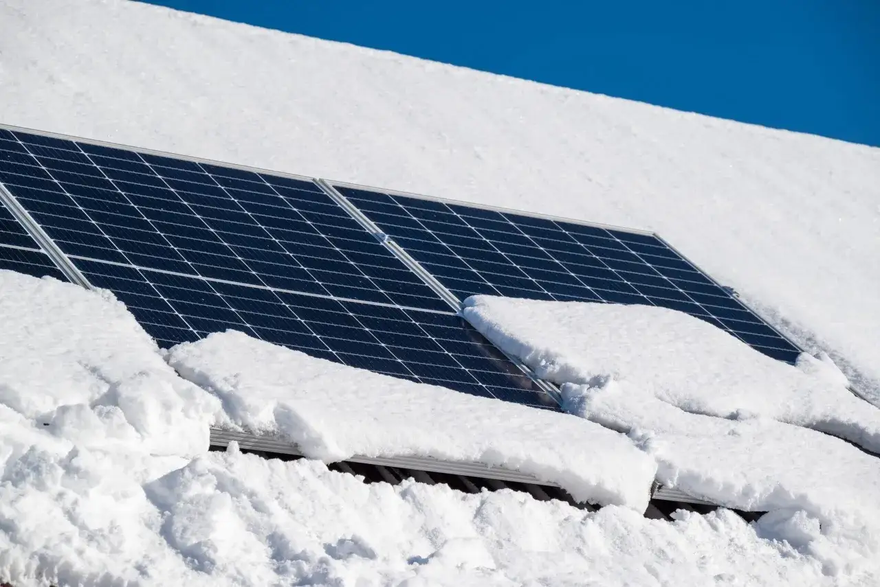 Solceller t&auml;ckta av sn&ouml; p&aring; ett tak en klar vinterdag. Trots sn&ouml;n kan solceller fortfarande producera energi.
