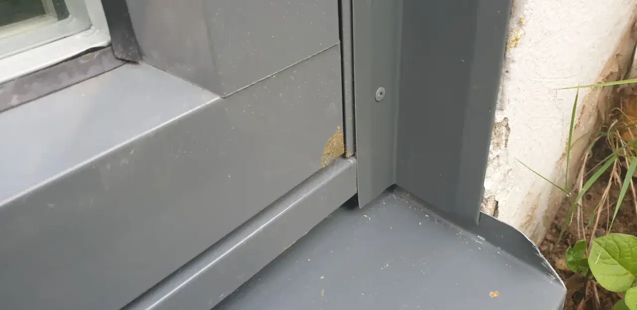 Gr&aring; pl&aring;t runt ett f&ouml;nster med en liten fl&auml;ck av gulaktigt, l&aring;gexpanderande fogskum i h&ouml;rnet.