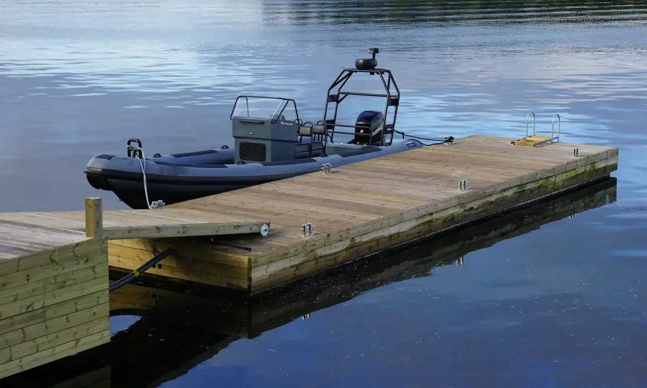 En gr&aring; RIB-b&aring;t ligger f&ouml;rt&ouml;jd vid en nybyggd flytbrygga. Perfekt f&ouml;r att bygga flytbrygga och njuta av vattnet.