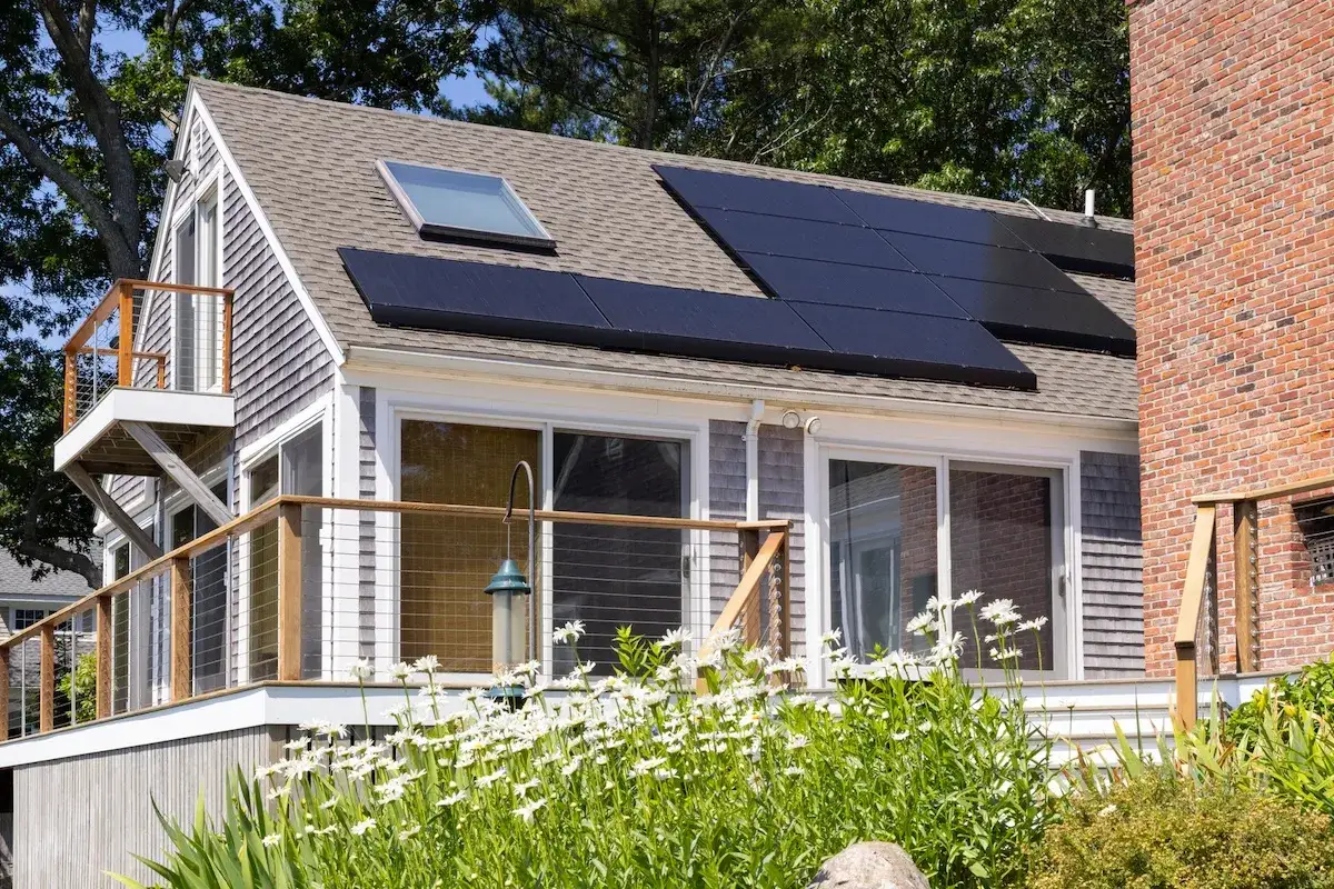 Hus med solceller p&aring; taket, omgivet av gr&ouml;nska och blommor. Ett bidrag till en gr&ouml;nare framtid.